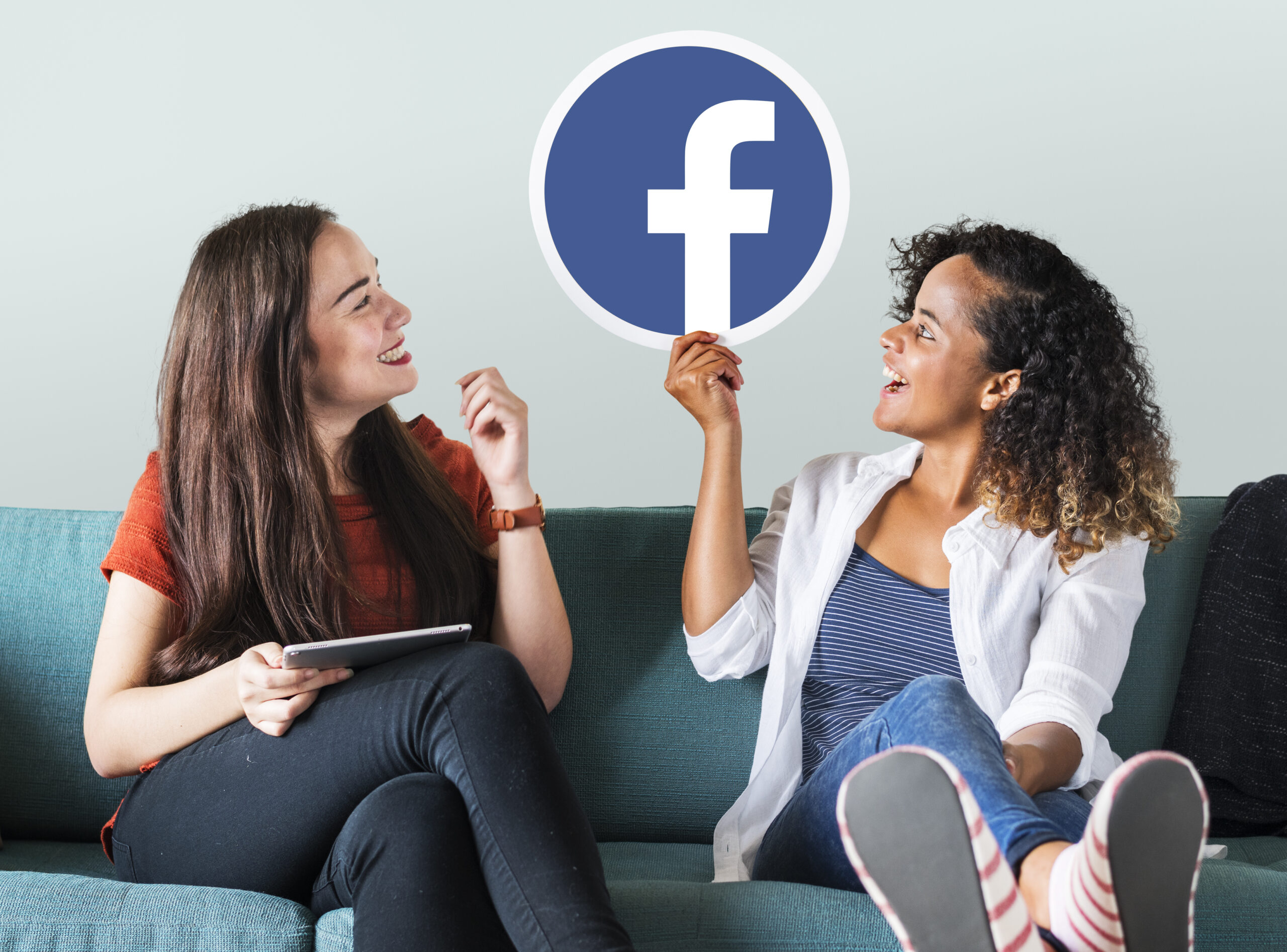 Two women laugh together as they scroll through Facebook